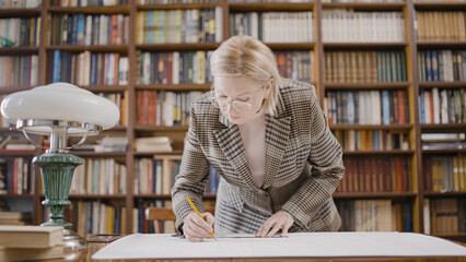 Female architect drawing a new blueprint project, working in a big office with books