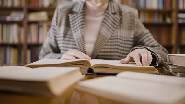 Close-up of mature woman reading a book, professor doing research in the library - Powered by Adobe