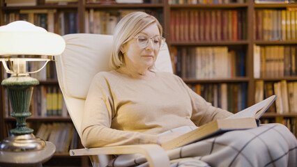 Beautiful senior woman reading a book in her cabinet, enjoying her hobby, feeling good