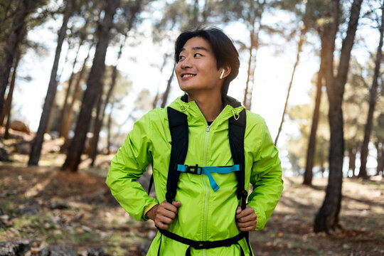 A young Asian man is hiking on top of a mountain. The man poses happily with his backpack while looking to the side. Concept of Koreans exercising,Asian hiking.