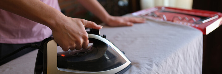 Female housewife ironing crumpled bedsheet on board using steam iron