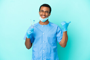 African American dentist holding tools over isolated blue background pointing to the side to present a product