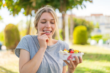 Young blonde woman holding a bowl of fruit at outdoors