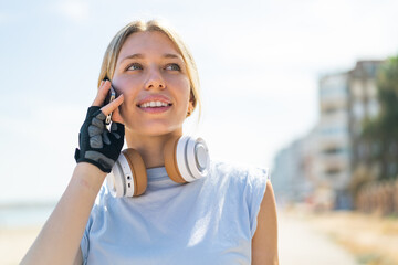 Young blonde woman at outdoors wearing sport wear and keeping a conversation with the mobile phone