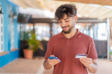 Young Arabian handsome man at outdoors buying with the mobile with a credit card