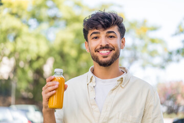 Fototapeta premium Young Arabian handsome man holding an orange juice at outdoors smiling a lot