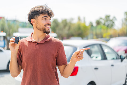 Young Arabian handsome man holding car key at outdoors pointing to the side to present a product