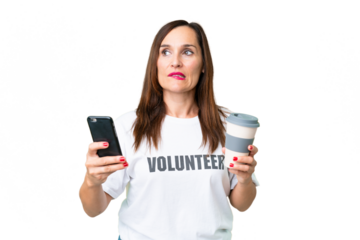 Middle age volunteer woman over isolated chroma key background holding coffee to take away and a mobile while thinking something