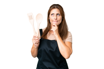 Middle age caucasian woman holding a rolling pin over isolated background having doubts and thinking