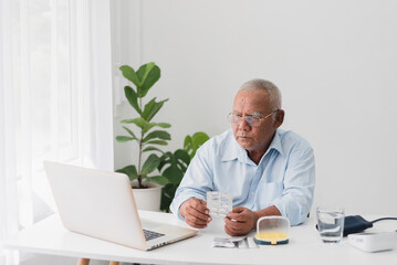 telemedicine and home health care concept, asian senior man worried and video conference with doctor at a table with a laptop computer at home.
