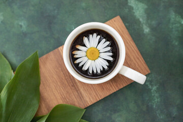 A cup of aromatic delicious coffee in a white cup on a green background. Daisies nearby