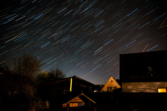 Long exposure picture of startrails and airplane trails at night over houses.