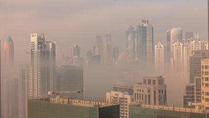 Dubai skyscrapers covered by morning fog in business bay district during sunrise timelapse.