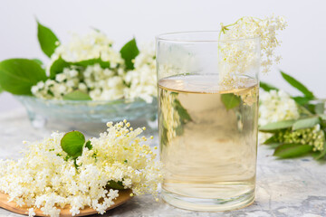 Homemade elderflower drink with sugar and lemon in a glass, light background