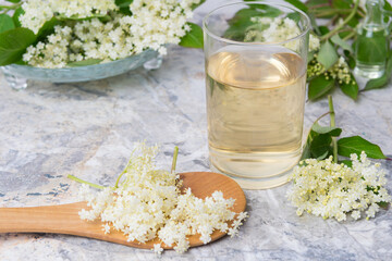 Homemade elderflower drink with sugar and lemon in a glass, light background