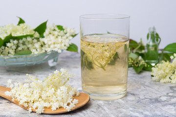 Homemade elderflower drink with sugar and lemon in a glass, light background