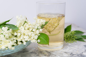 Homemade elderflower drink with sugar and lemon in a glass, light background