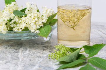 Homemade elderflower drink with sugar and lemon in a glass, light background