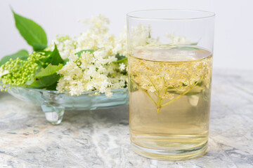 Homemade elderflower drink with sugar and lemon in a glass, light background