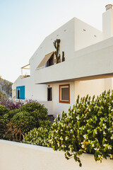 Fototapeta premium Front view of white facade of beach holiday apartment building. White and blue facade with trees and cactus with sunset light.