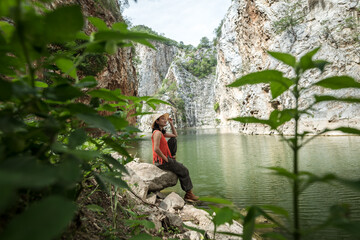 Beautiful smiling mature woman sitting next to lake. Enjoying the nature. Fresh outdoor woods, wellness healthy lifestyle concept. Summer country vacation.