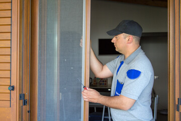 Image of a handyman installing a fly screen in a French window of his house. Protection of the house from insects.
