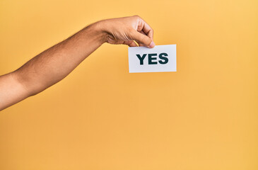 Hand of caucasian man holding paper with yes word over isolated yellow background