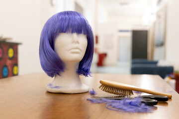 purple wig resting on a styrofoam head of a mannequin with a comb and scissors used to cut hair in...
