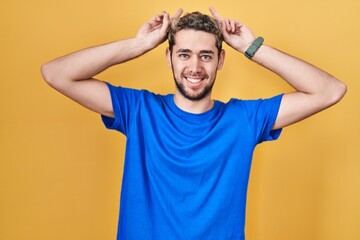 Fototapeta na wymiar Hispanic man with beard standing over yellow background posing funny and crazy with fingers on head as bunny ears, smiling cheerful