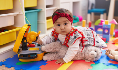 Fototapeta na wymiar Adorable hispanic baby sitting on floor with relaxed expression at kindergarten