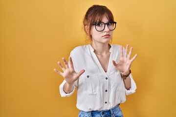 Young beautiful woman wearing casual shirt over yellow background moving away hands palms showing refusal and denial with afraid and disgusting expression. stop and forbidden.