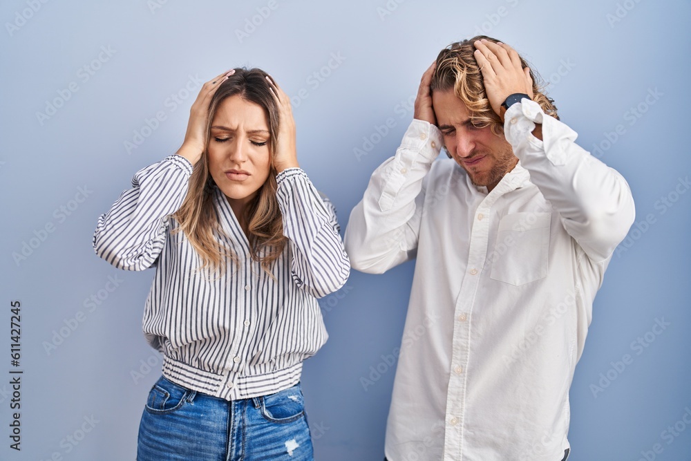 Wall mural Young couple standing over blue background suffering from headache desperate and stressed because pain and migraine. hands on head.