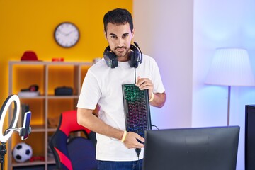 Young hispanic man streamer smiling confident holding keyboard computer at gaming room