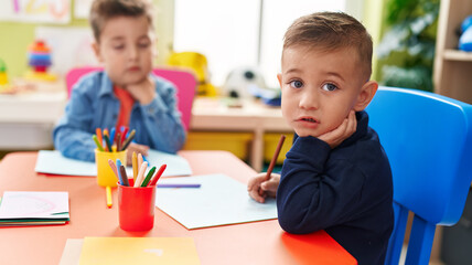Adorable boys preschool students sitting on table drawing on paper at kindergarten
