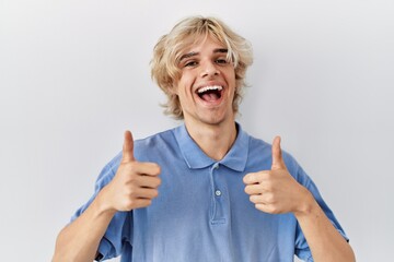 Young modern man standing over isolated background success sign doing positive gesture with hand, thumbs up smiling and happy. cheerful expression and winner gesture.