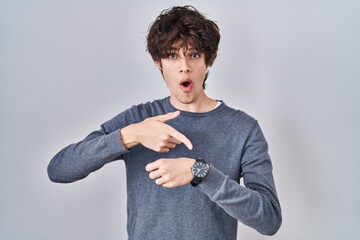Young man standing over isolated background in hurry pointing to watch time, impatience, upset and...