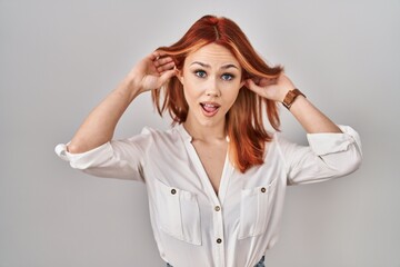 Young caucasian woman standing over isolated background smiling pulling ears with fingers, funny...