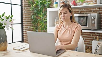 Young blonde woman using laptop sitting on table at dinning room