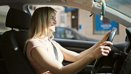 Fototapeta na wymiar Young blonde woman smiling confident driving car at street