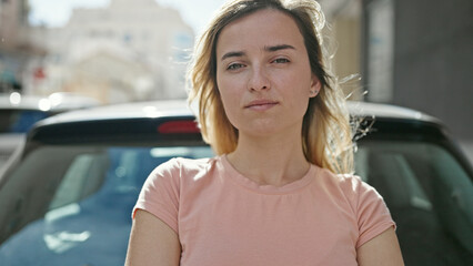 Young blonde woman standing by car with arms crossed gesture at street