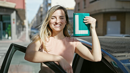 Young blonde woman smiling confident holding new driver license at street