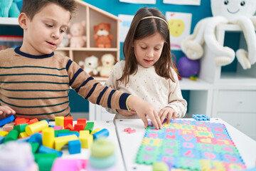 Adorable boy and girl playing with construction blocks and vocabulary puzzle at kindergarten