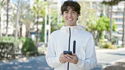 Young hispanic man using smartphone smiling at park