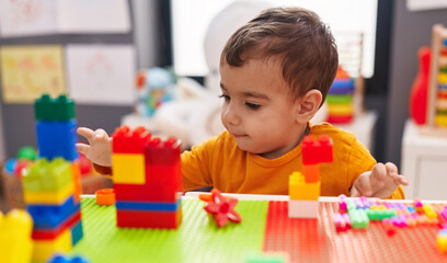 Adorable hispanic boy playing with construction blocks sitting on table at kindergarten