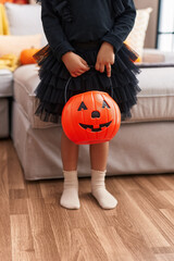 Adorable hispanic girl having halloween party holding pumpkin basket at home