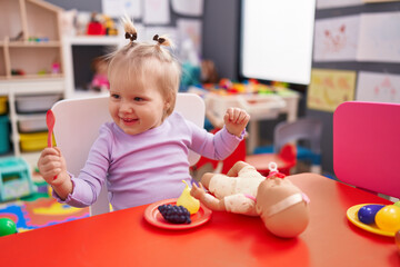 Adorable blonde girl playing to eat sitting on table at kindergarten