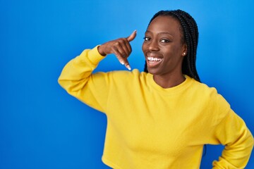 Beautiful black woman standing over blue background smiling doing phone gesture with hand and fingers like talking on the telephone. communicating concepts.