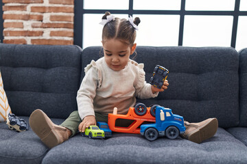 Adorable hispanic girl playing with car toy sitting on sofa at home