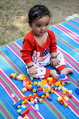 Fototapeta na wymiar Cute little Indian infant sitting enjoying outdoor shoot at society park in Delhi, Cute baby boy sitting on colourful mat with grass around, Baby boy outdoor shoot