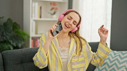Young blonde woman listening to music sitting on the sofa singing song at home